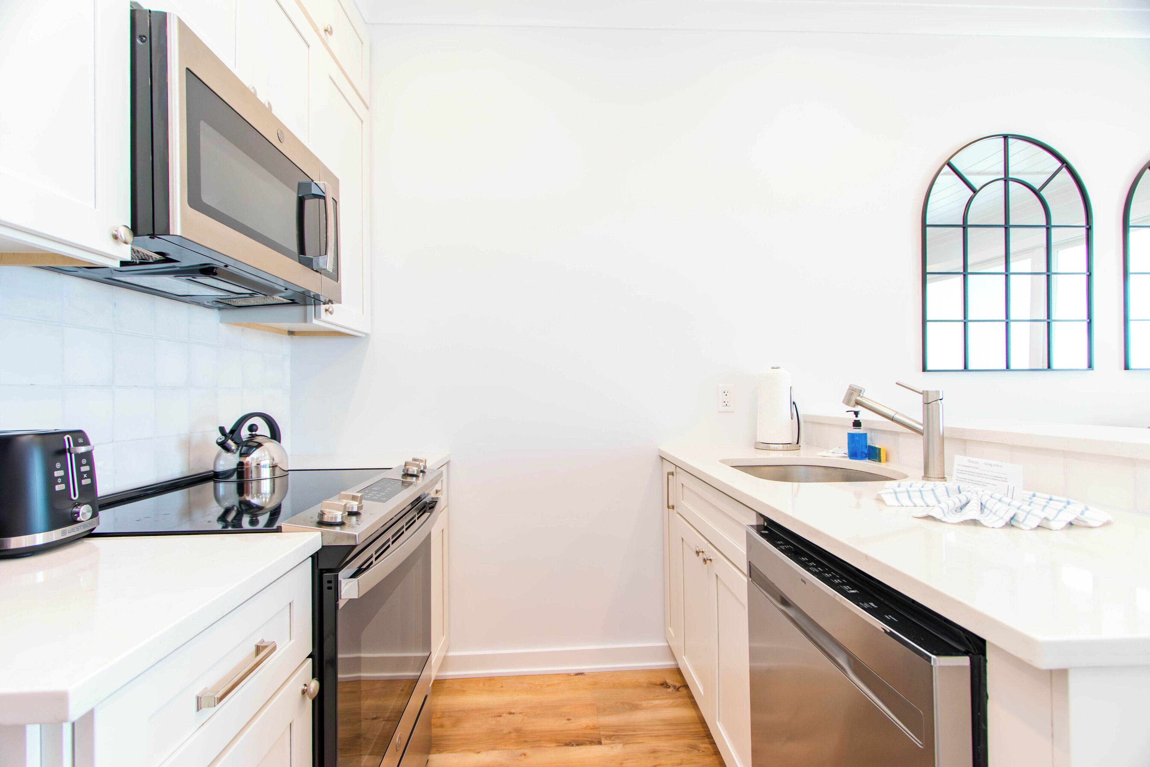 A compact kitchen with a microwave, toaster, kettle, and dishwasher.