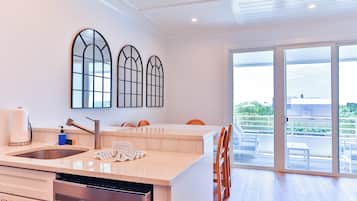 A modern kitchen with a dishwasher, a sink, and a large island with chairs. There are three arched windows on the wall and a sliding glass door leading to an outdoor area.