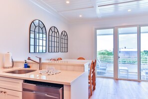 Una cocina moderna con lavavajillas, un lavamanos y una isla grande con sillas. Hay tres ventanas arqueadas en la pared y un ventanal corredero que da a un espacio exterior.