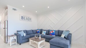 Ett modernt vardagsrum med en grå soffa, ett soffbord i trä och en väggmonterad skylt med texten ”BEACH”.