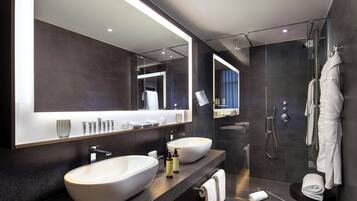 A modern bathroom with a large mirror, two sinks, a shower, and a towel rack.