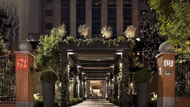 A hotel entrance with a covered walkway, large potted plants, and illuminated signage. - ME Milan - Il Duca (Milan)
