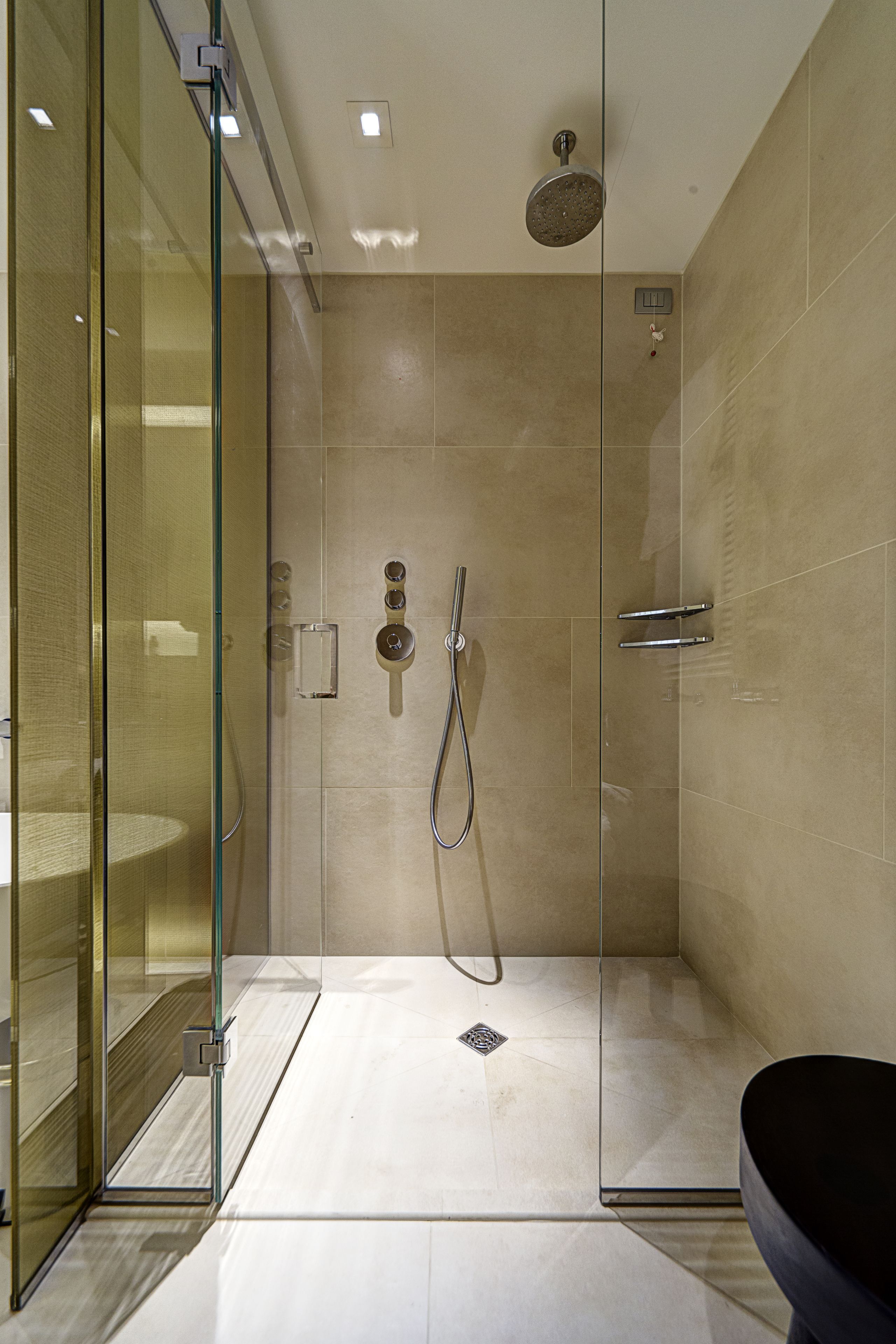 A modern shower area with a glass door, a handheld showerhead, and a wall-mounted faucet.