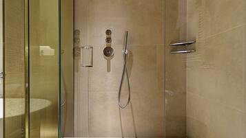 Un baño moderno con mampara de vidrio, ducha de mano y panel de control en la pared.