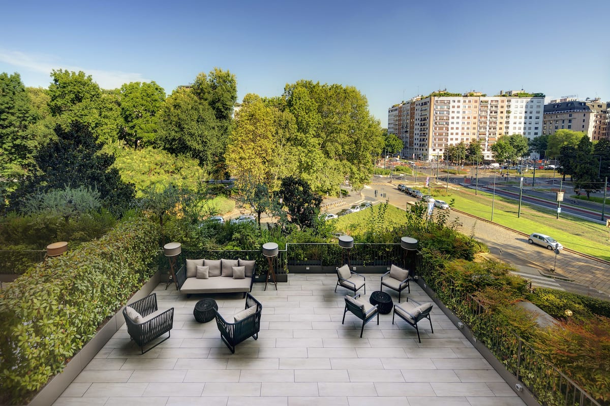 A rooftop patio with outdoor furniture, a view of a cityscape, and a road with vehicles.