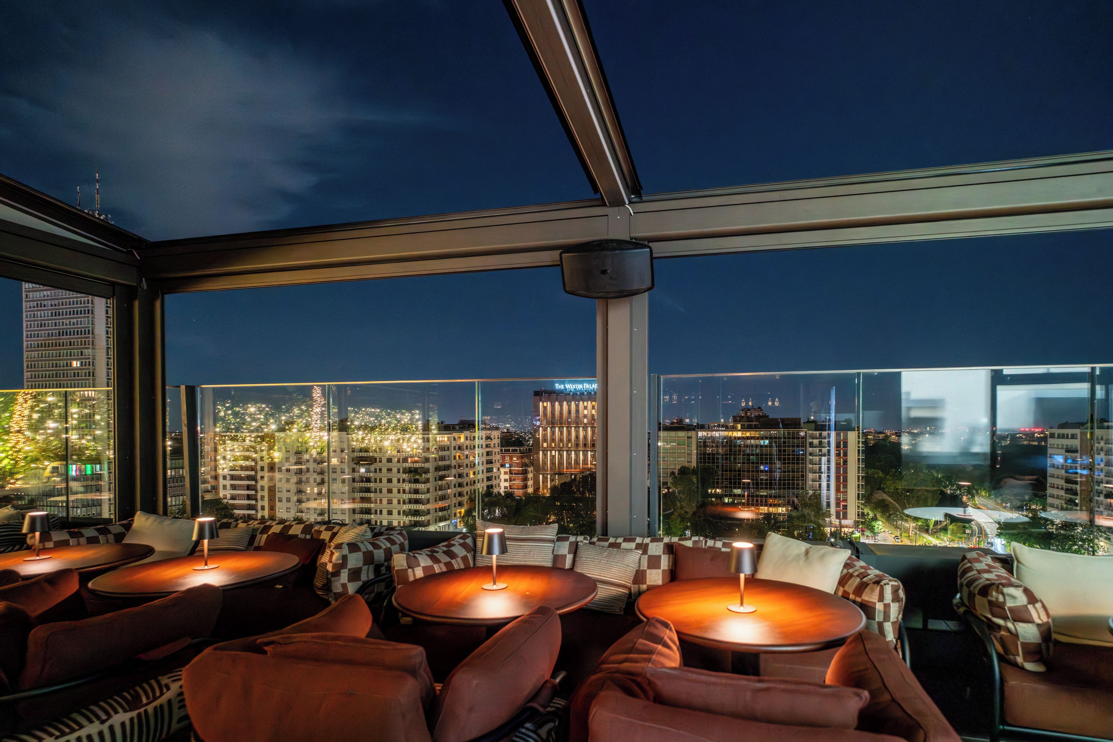 A rooftop bar with multiple seating areas and a city view.