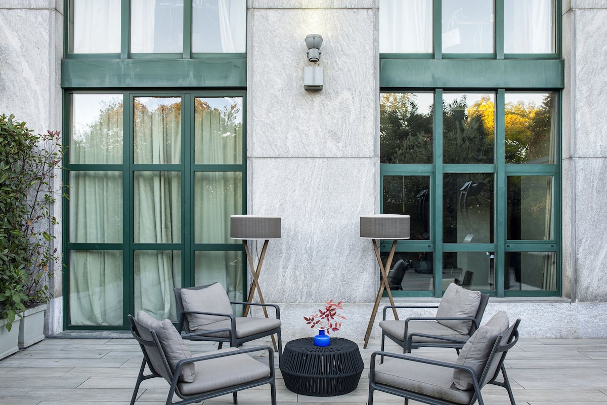 A patio area with four grey chairs, two floor lamps, and a round table with a vase of red flowers.