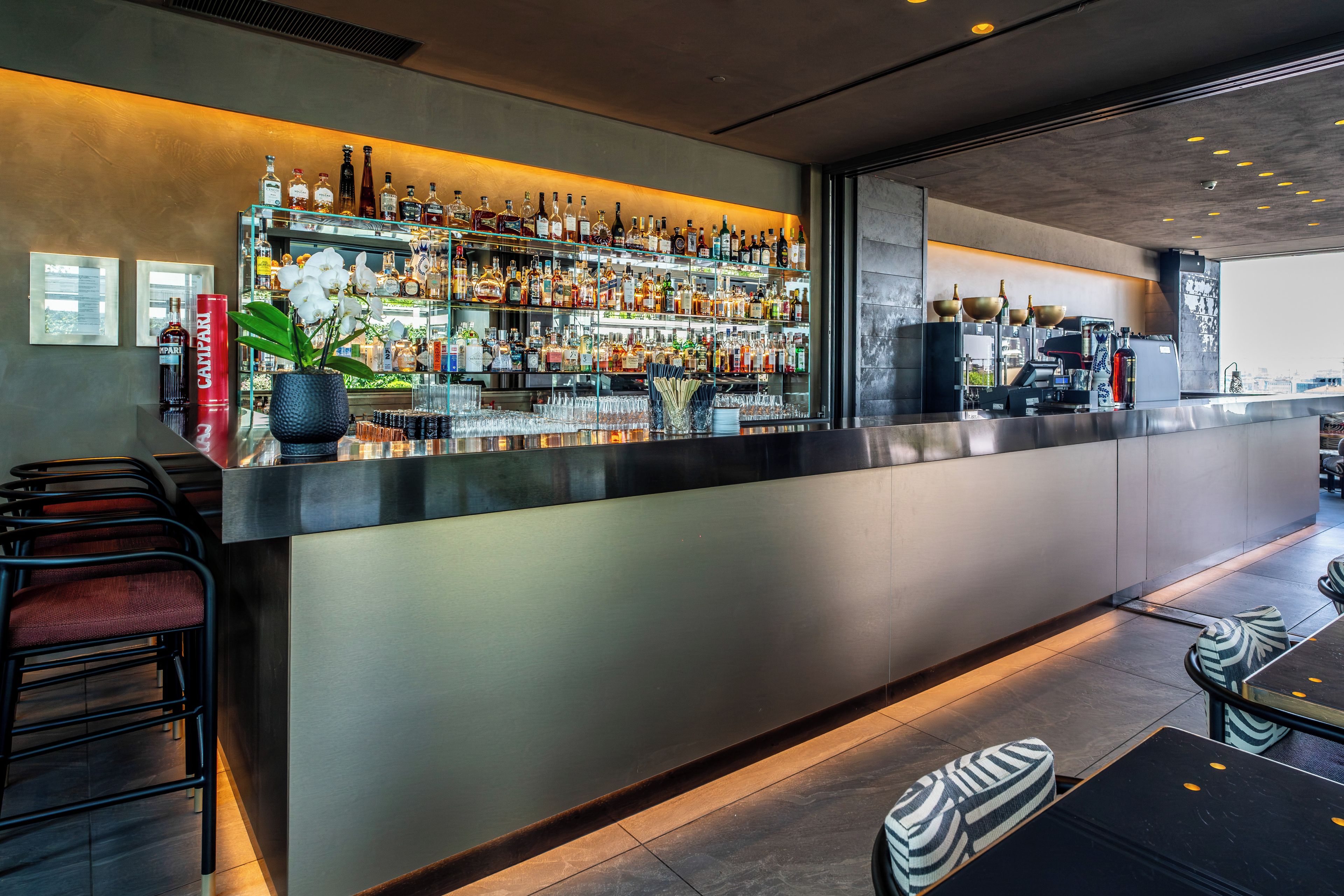 Eine Bar mit einer langen Theke, Regalen voller Spirituosen und Sitzgelegenheiten mit Hockern.