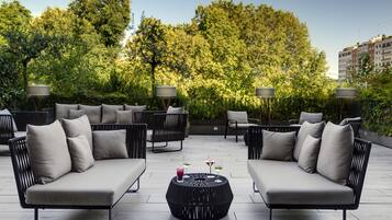 Una terrazza sul tetto con mobili da esterno, inclusi divani e poltrone, e due tavoli rotondi con bevande.