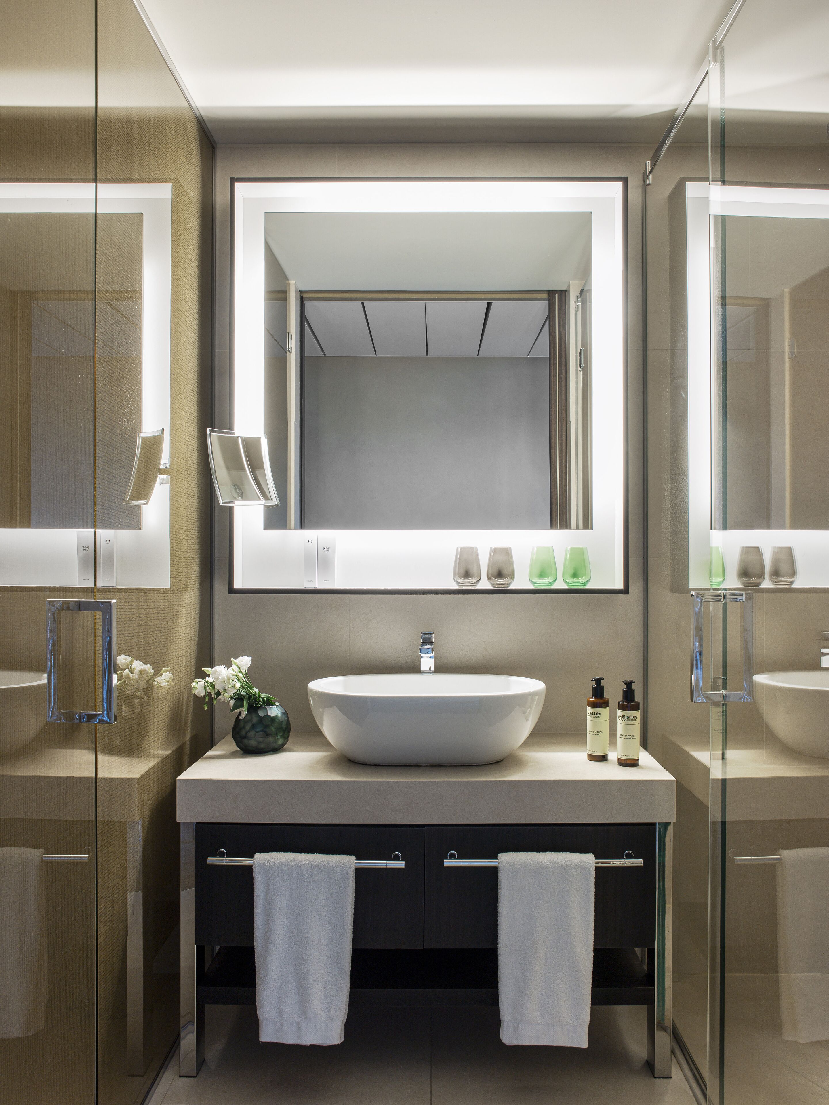 Un baño moderno con un espejo grande, un lavamanos central y dos toalleros.