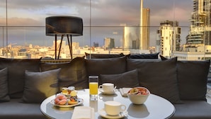 A high-rise room with a city view, a round dining table with breakfast items, and a modern lamp. - ME Milan - Il Duca (Milan)