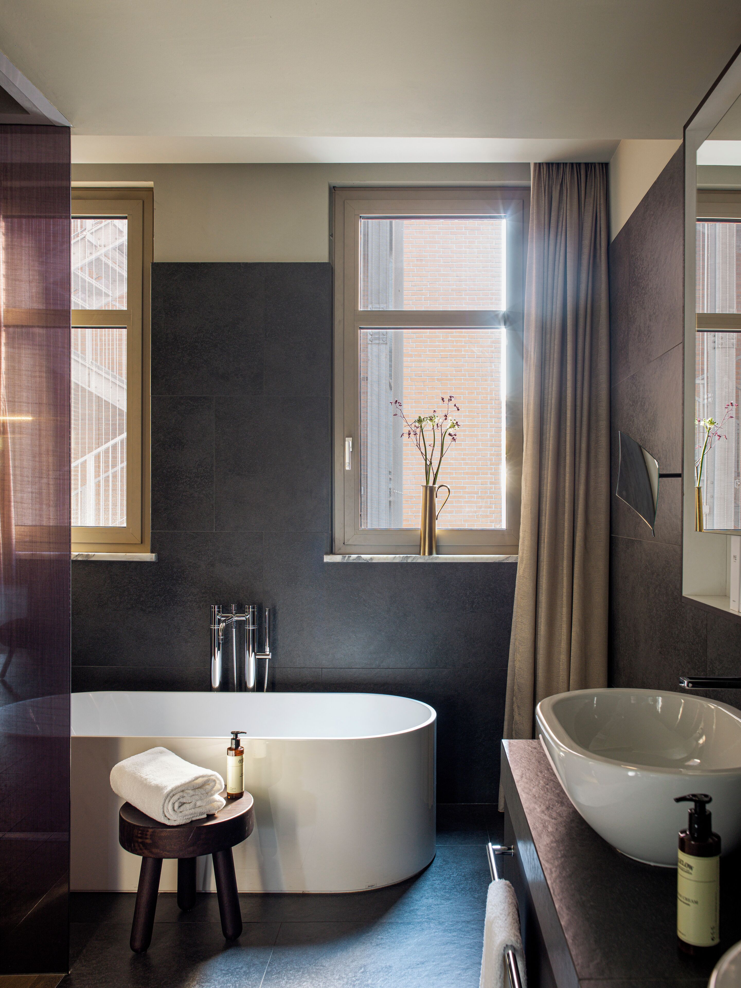 A modern bathroom with a freestanding bathtub, a large sink, and a window with curtains.