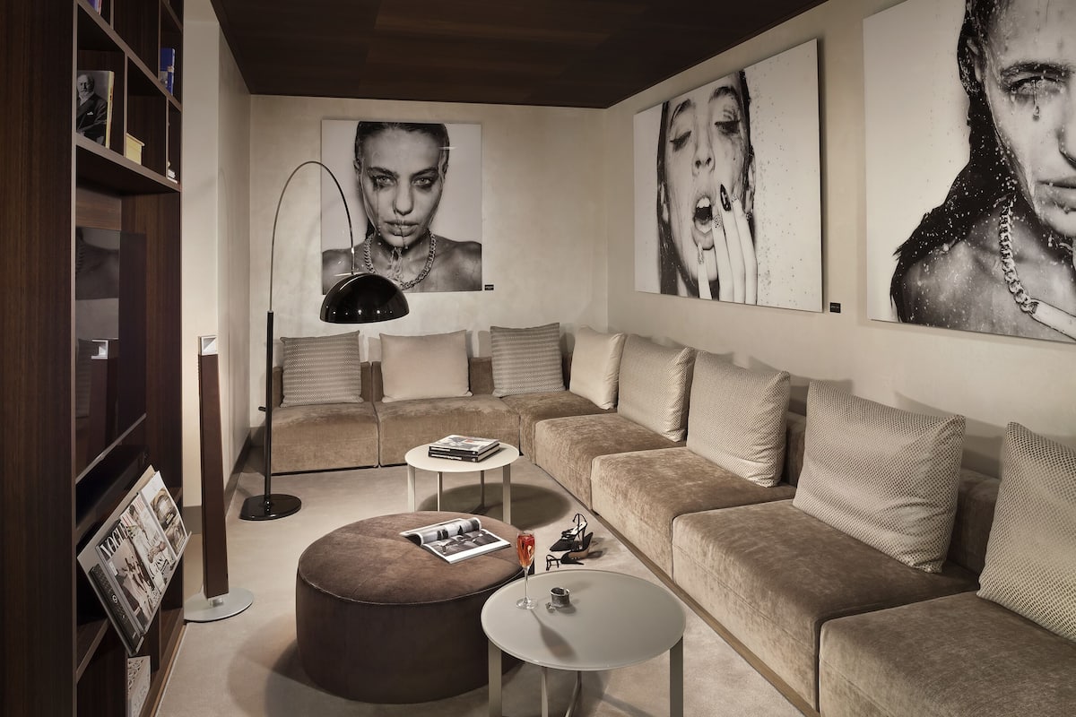 A modern living room with a sectional sofa, a round ottoman, a small coffee table, a floor lamp, and a bookshelf.