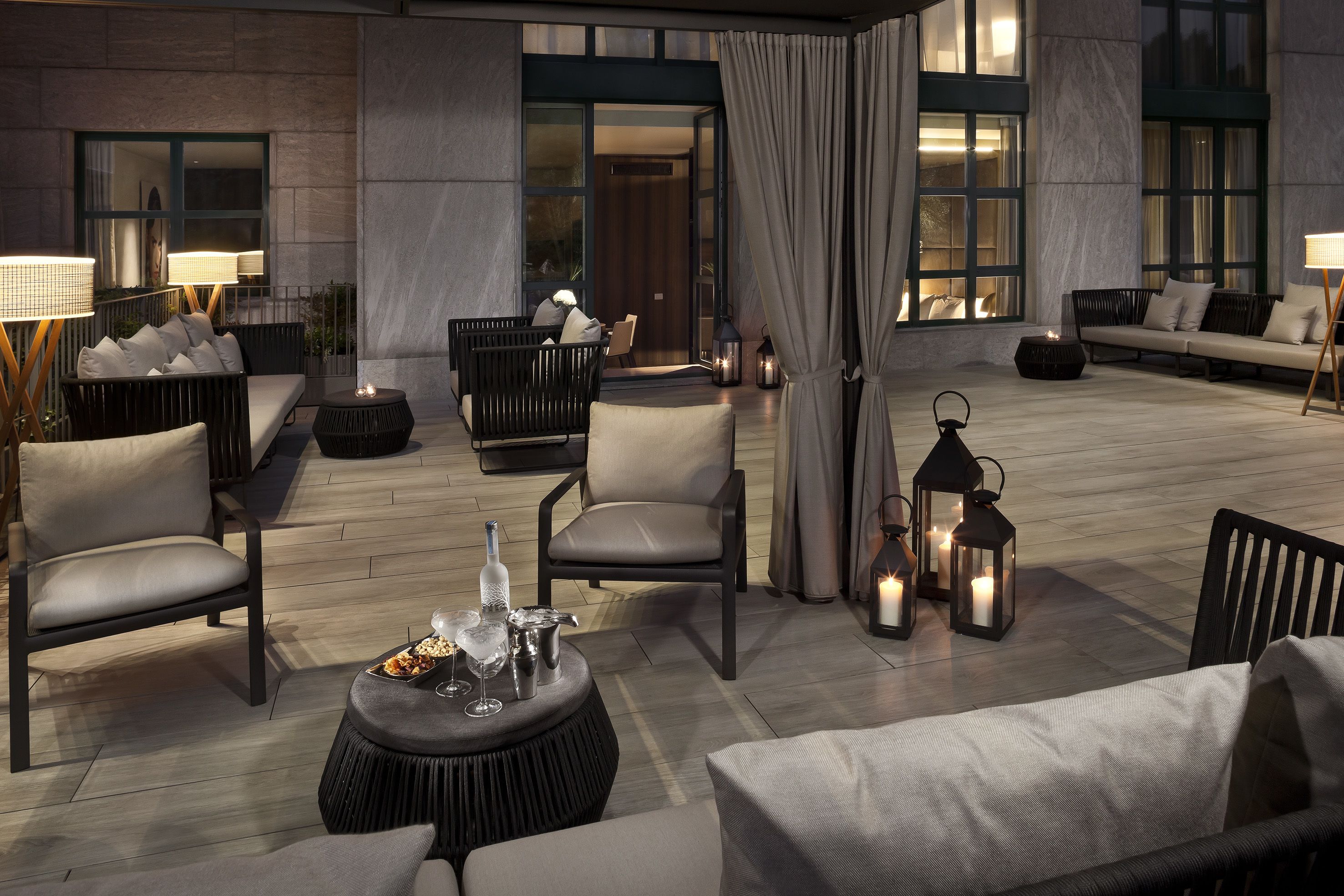 A modern outdoor seating area with comfortable chairs, a round table with drinks, and ambient lighting.
