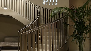 A modern staircase with a curved design, a potted plant, and a wall with the text "STK MILAN". - ME Milan - Il Duca (Milan)