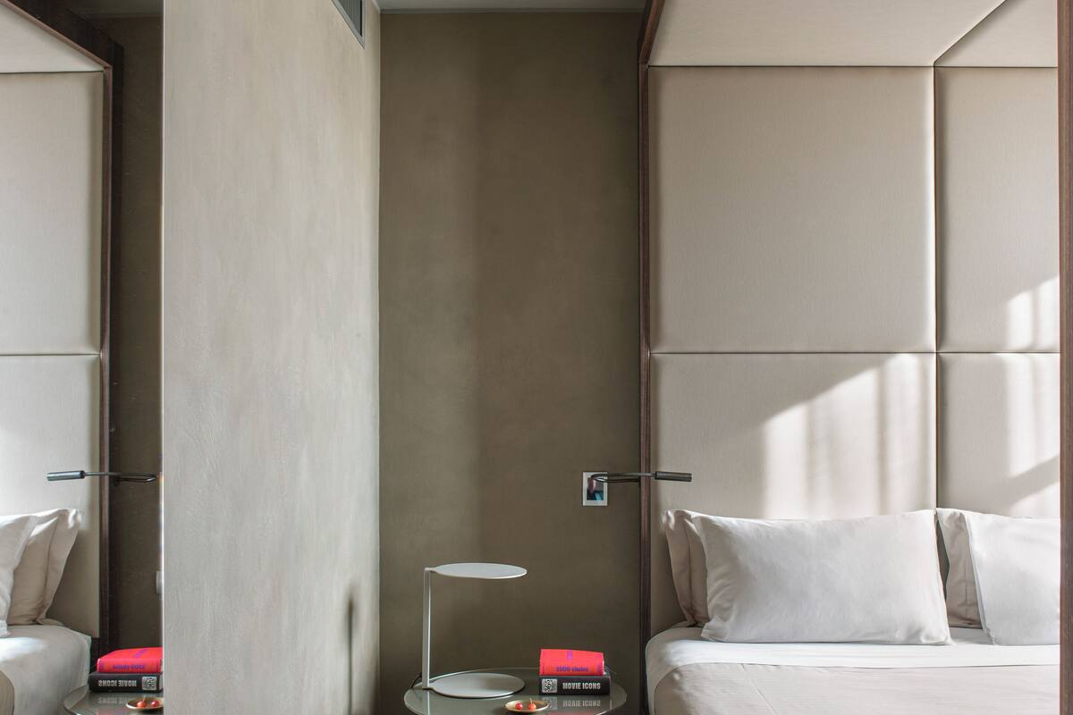 A hotel room with a bed, a bedside table with a lamp, and a small table with books.