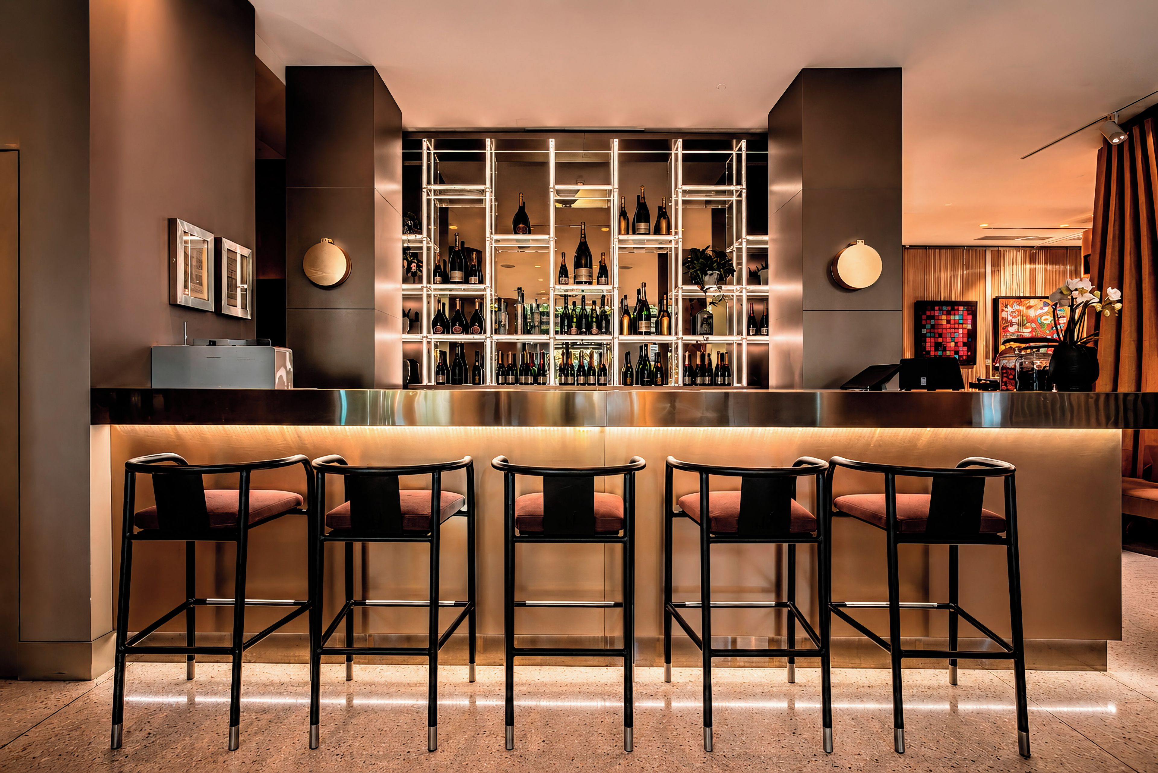 A bar area with a counter, multiple shelves of bottles, and three bar stools.