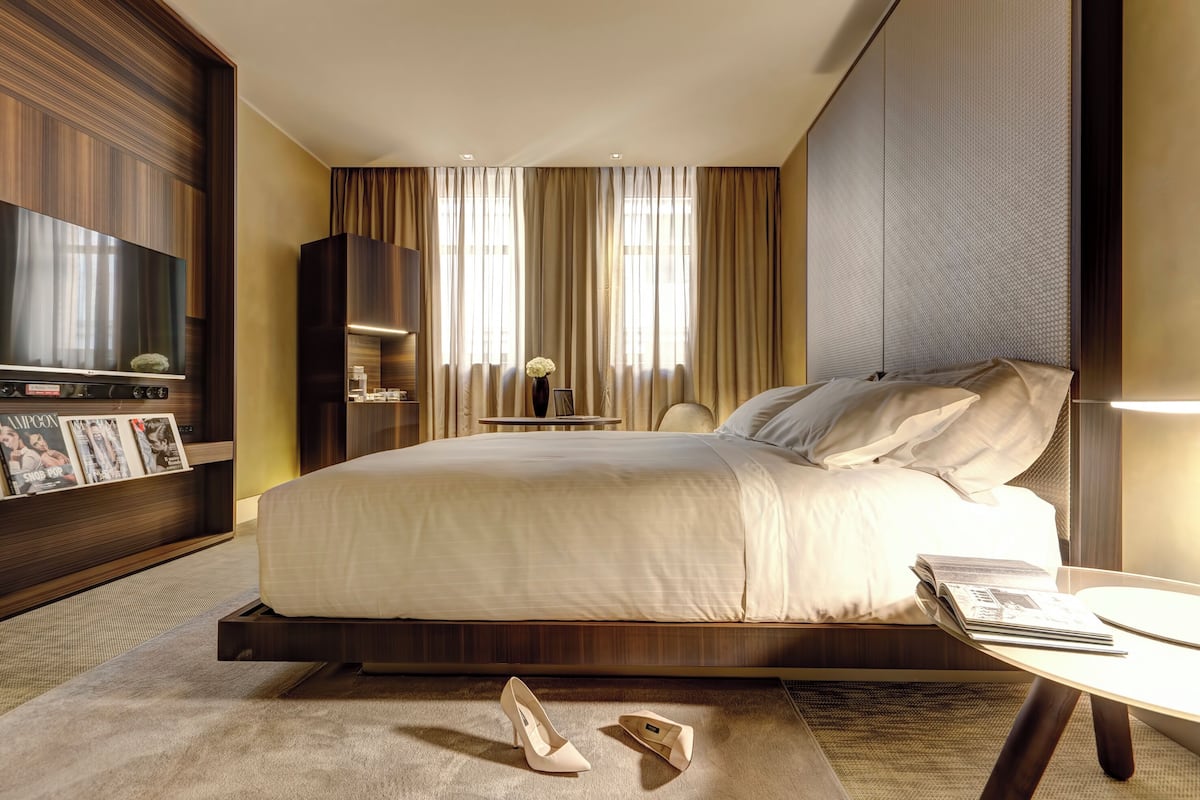 A modern hotel room with a large bed, a flat-screen TV, a bedside table, and a small side table with a vase.