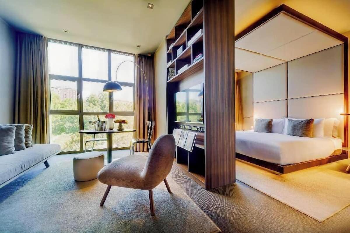 A modern hotel room with a sofa, a chair, a bed, a TV, and a table with a lamp.