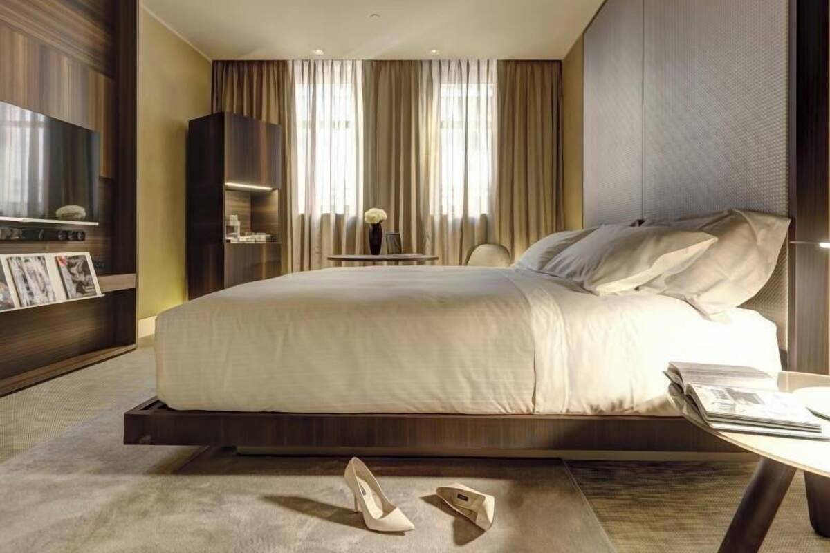A modern hotel room with a large bed, a flat-screen TV, a small table, and a chair.