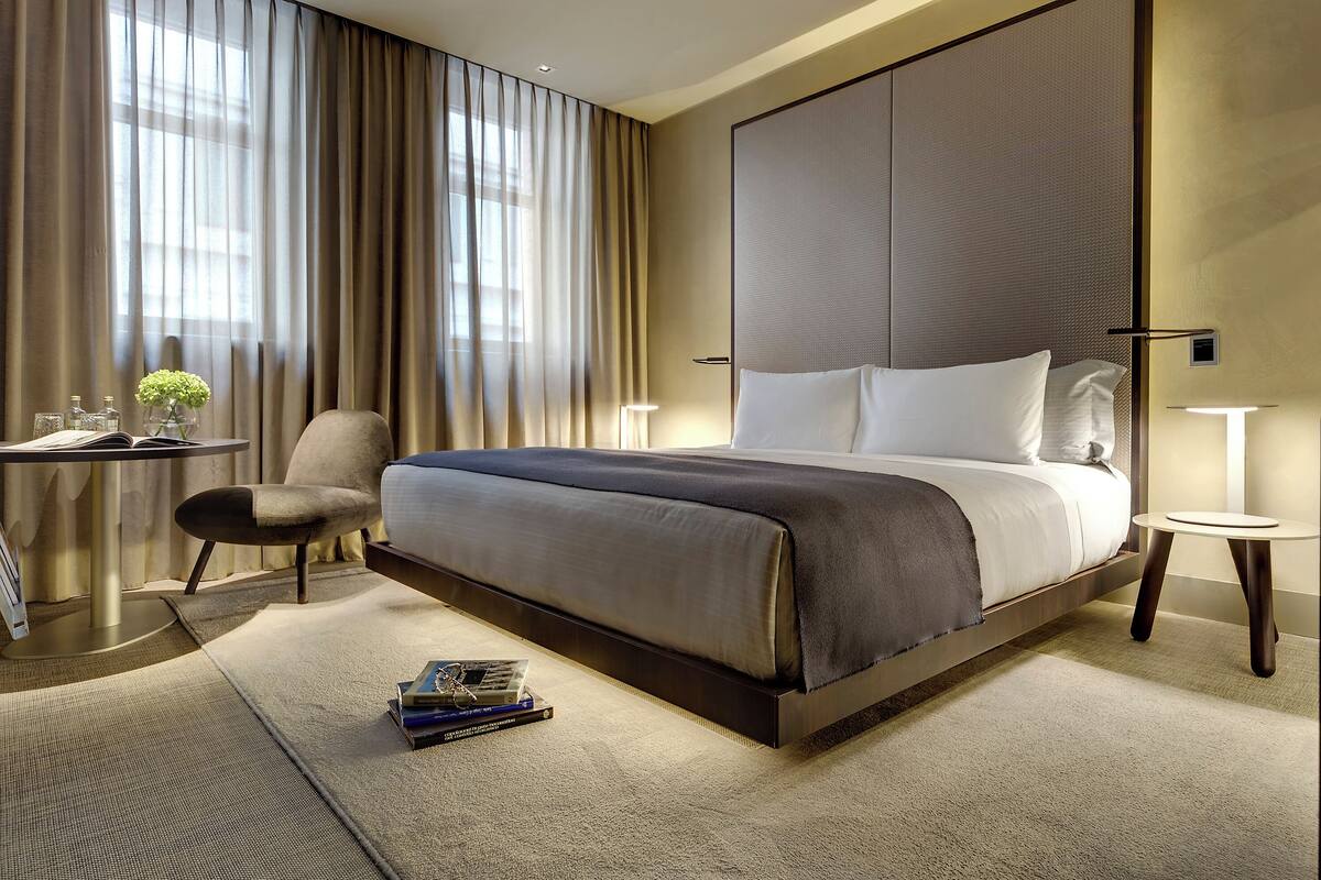A modern hotel room with a large bed, a desk, and a chair.