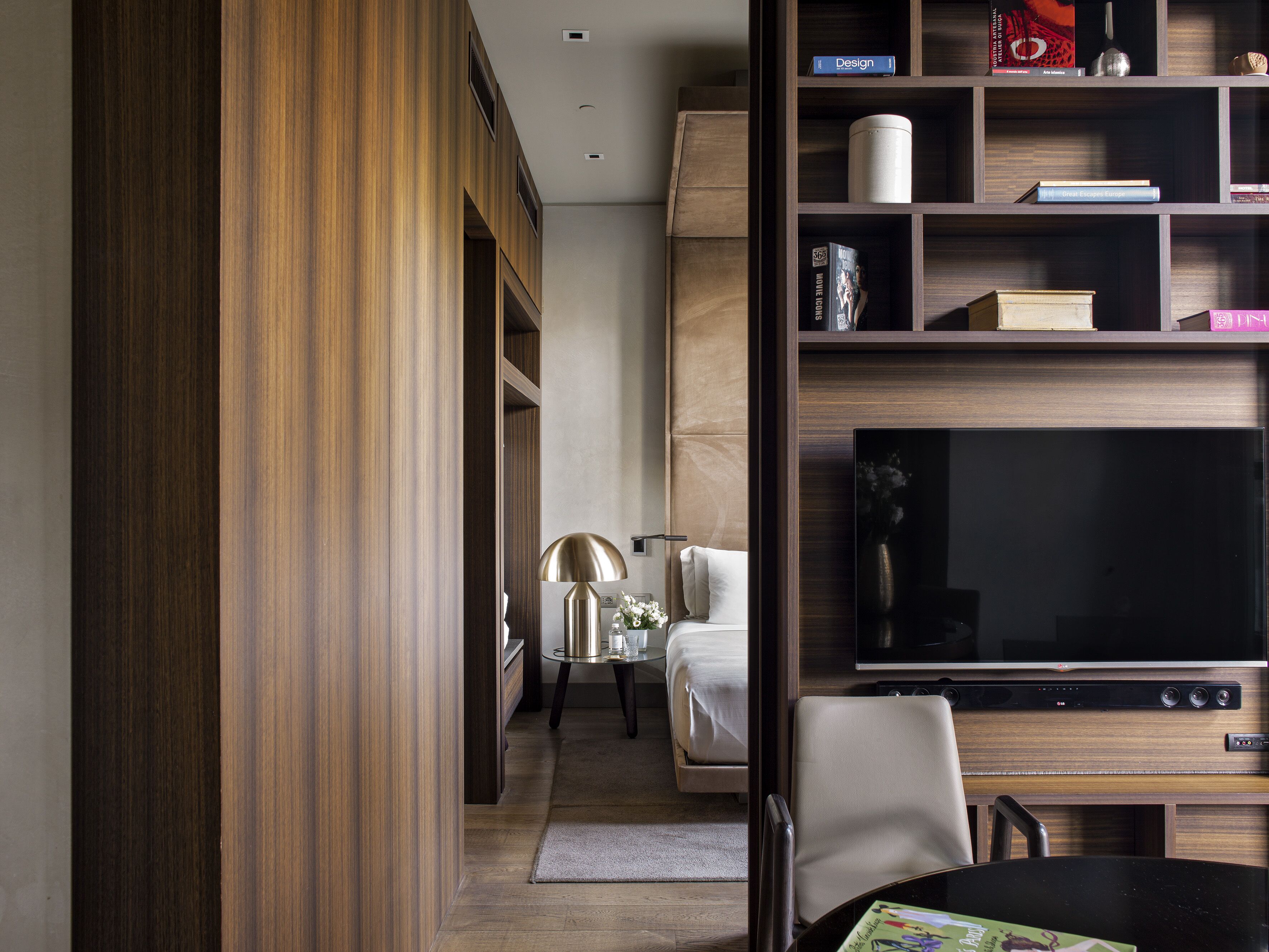 Una habitación de hotel moderna con un armario de madera, un televisor de pantalla plana, un sofá y una mesa de comedor.