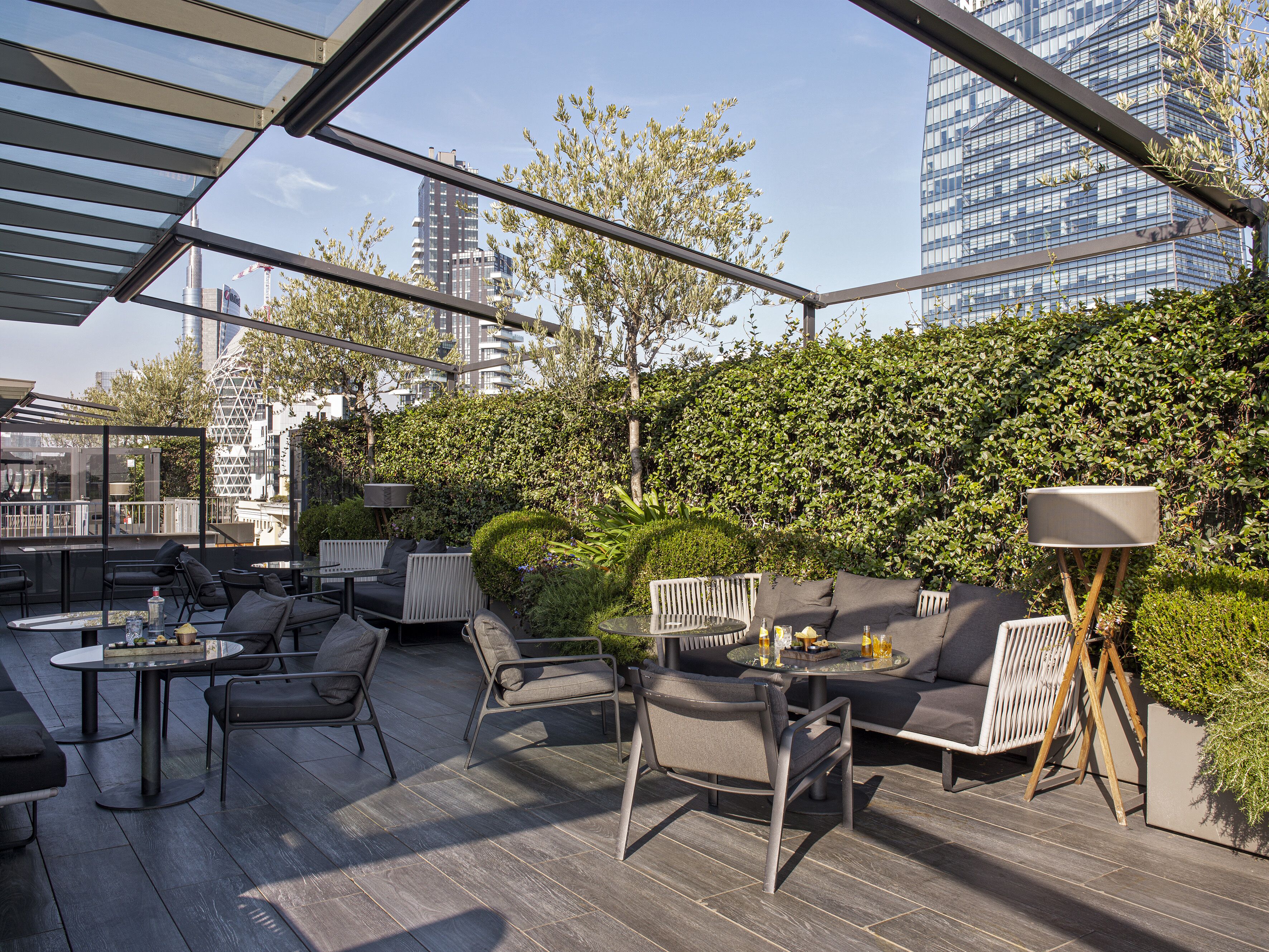 An outdoor seating area with modern furniture, a glass ceiling, and a view of city buildings.
