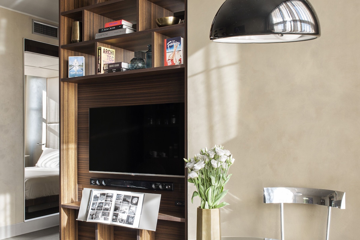 Uma sala de estar moderna com uma TV de tela plana, estantes de madeira, uma mesa de vidro e um vaso de flores.