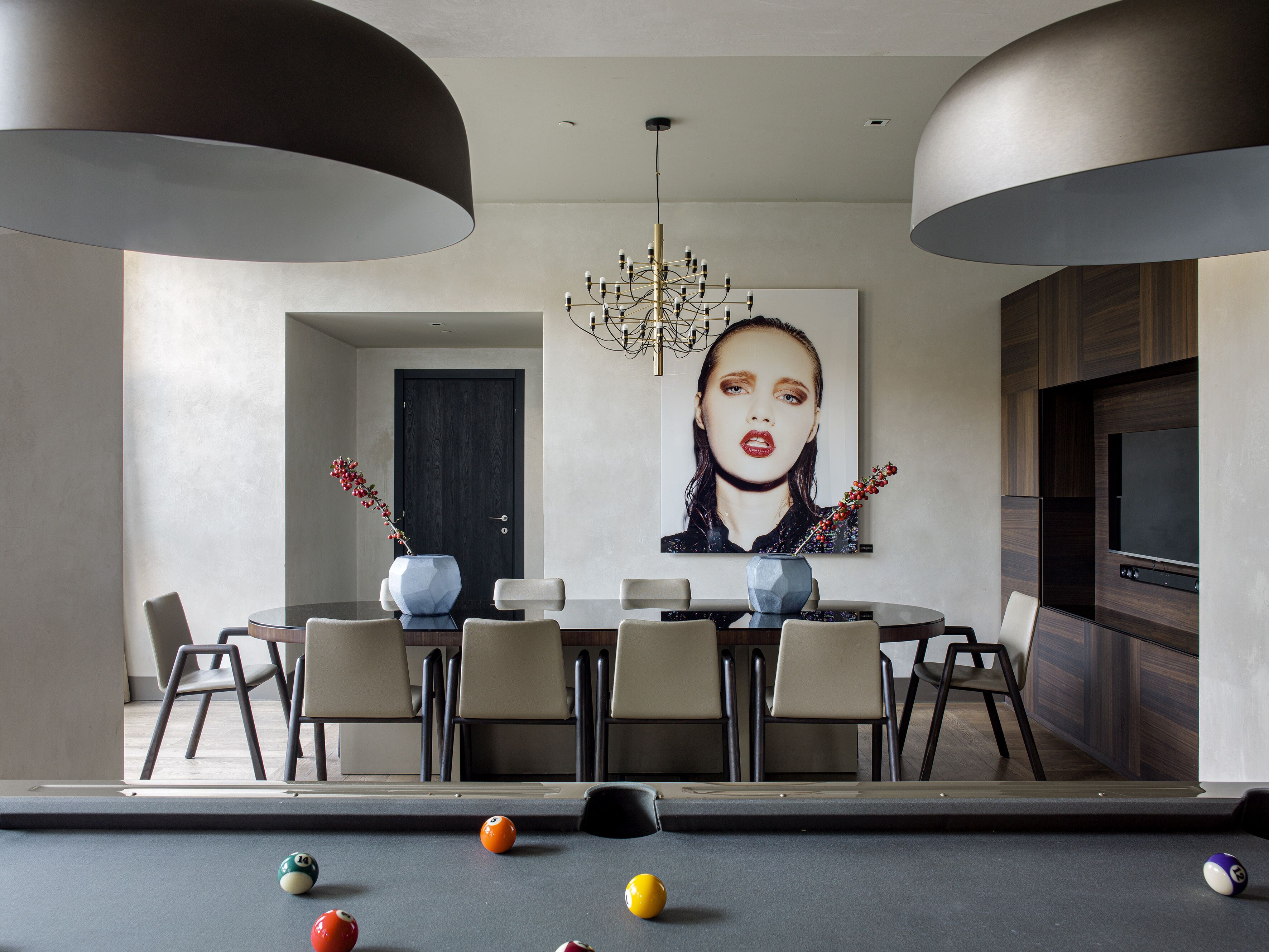 A modern dining area with a pool table, dining chairs, and a chandelier.