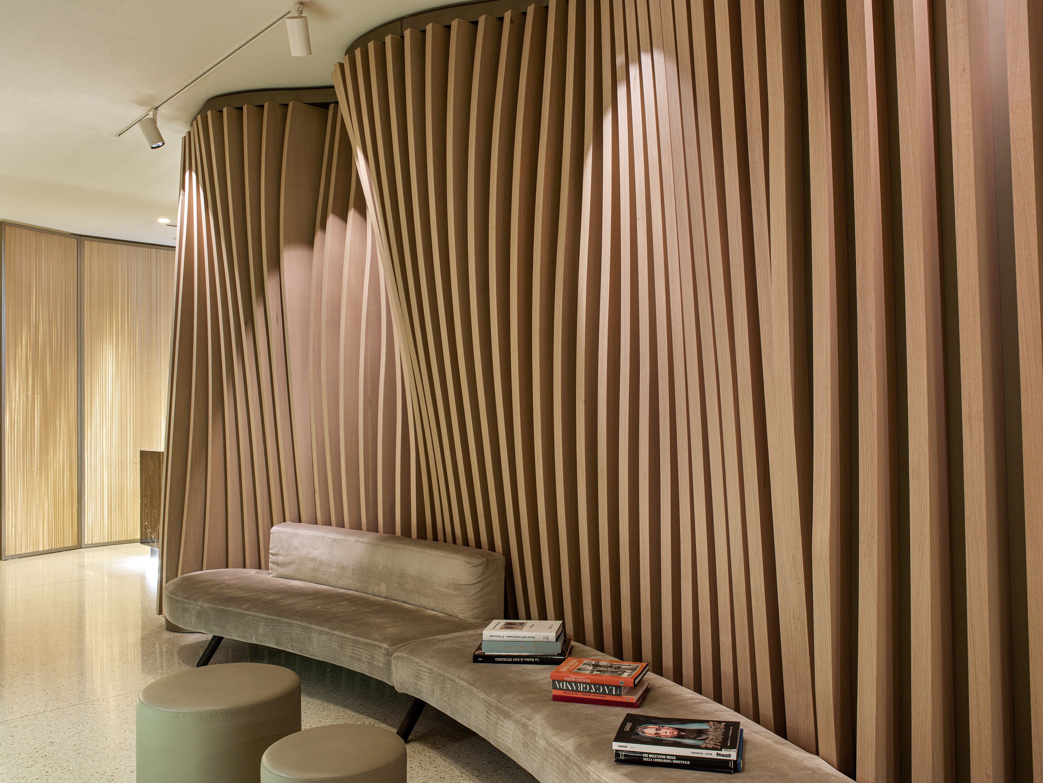 Ein modernes Interieur mit einer gebogenen Couch, einem kleinen Tisch mit Büchern und einer Wand mit vertikalen Holzlatten.