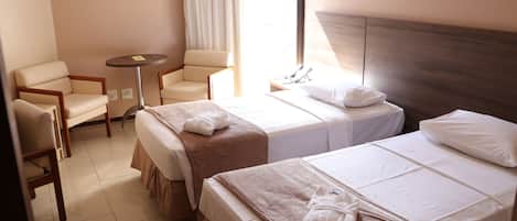 A hotel room with two beds, a small round table, a chair, and a bedside telephone.