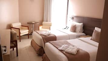 A hotel room with two beds, a sitting area with a chair and a small table, and a window with curtains.