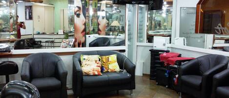 A salon interior with multiple black leather chairs, a television mounted on the wall, and a mirror reflecting the salon's interior.