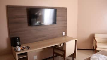 Ein Hotelzimmer mit einem Holztisch, einem an der Wand montierten Fernseher, einem Sessel, einem Bett und einer Kaffeemaschine.
