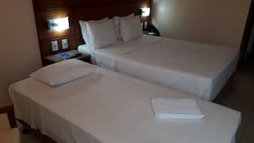Dos camas individuales con sábanas blancas, cabecero de madera, lámparas de noche y una toalla doblada en la cama de la derecha.