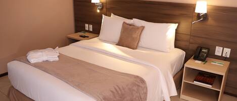 A hotel room with a large bed, two bedside tables, a nightstand, and a lamp.