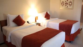 Two double beds with white linens and brown throw pillows, a bedside table with a lamp, and a framed artwork on the wall.