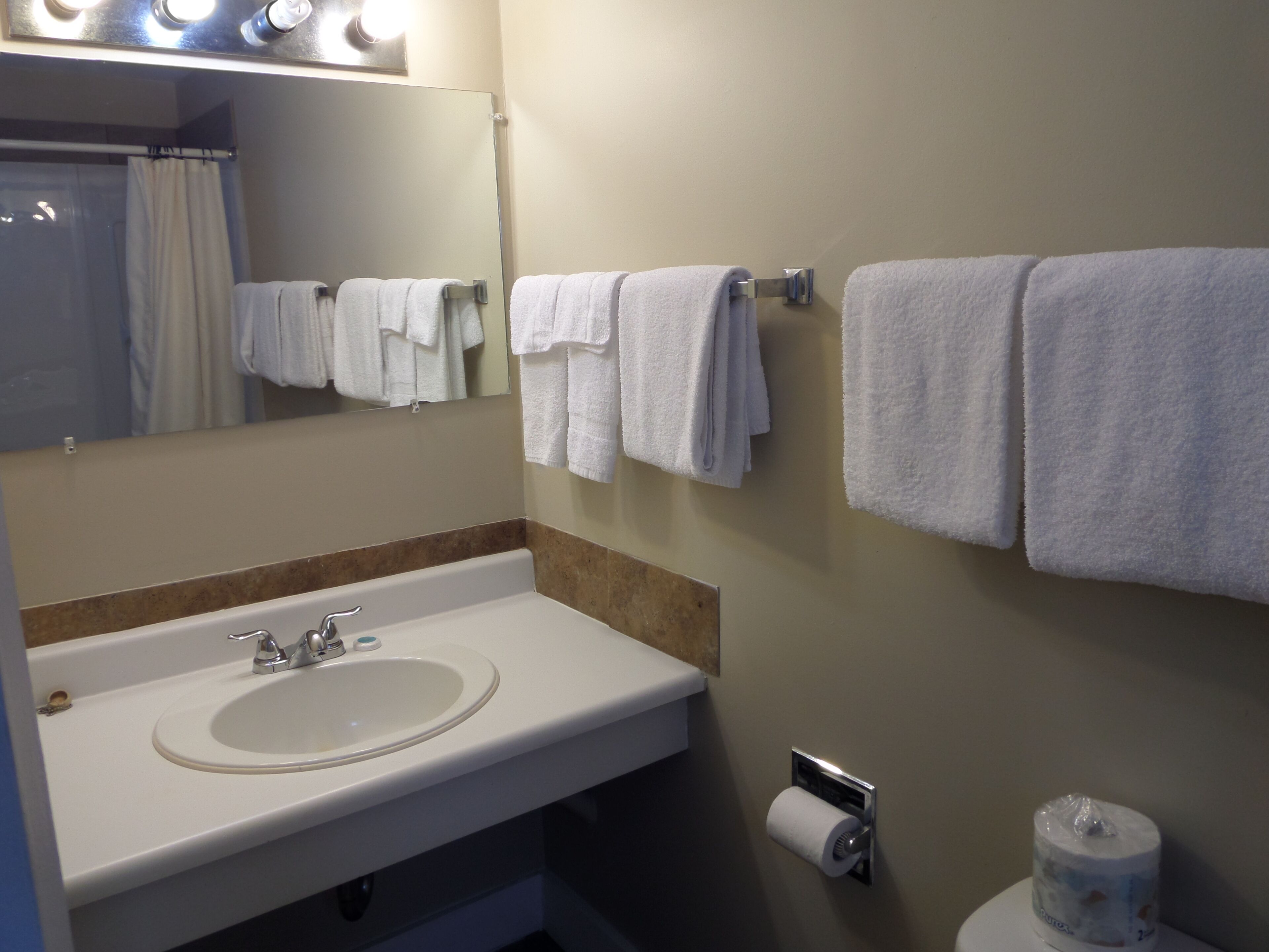 Un baño con lavamanos, espejo, toallero y dispensador de papel higiénico.