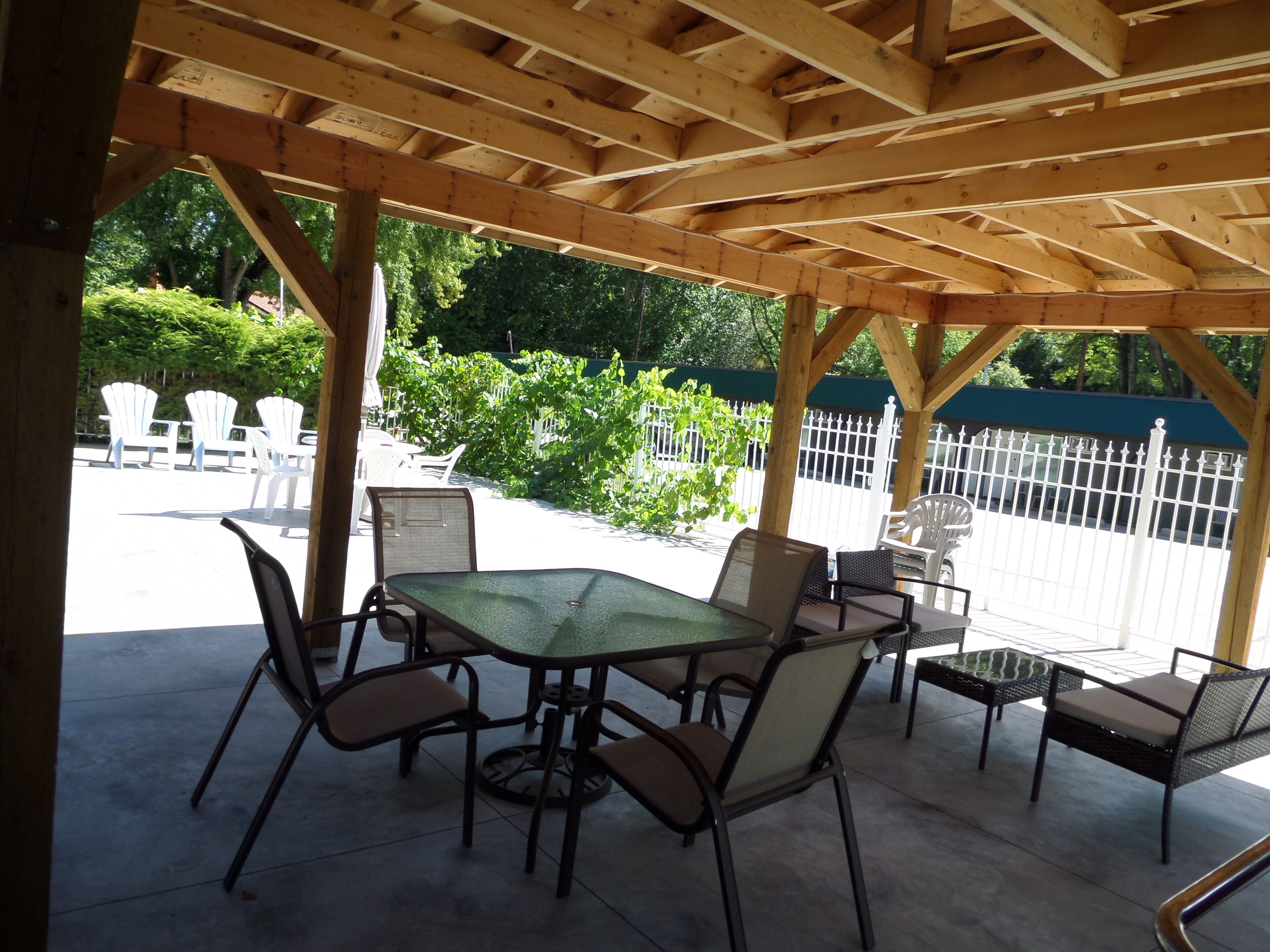 An outdoor patio with a wooden pergola, a glass-top table, and wicker chairs.
