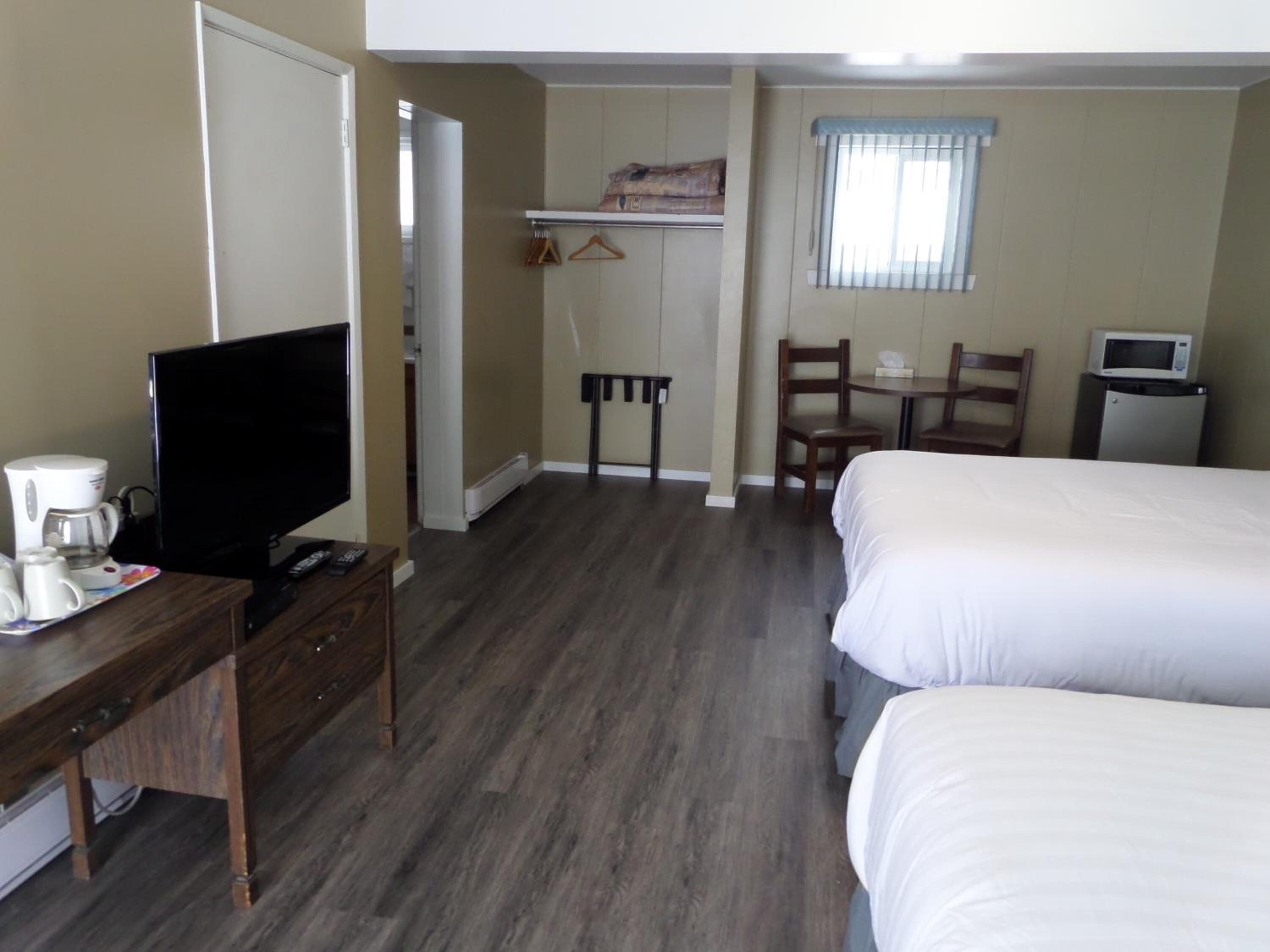 A hotel room with two beds, a TV, a desk with a coffee maker, a chair, a table, and a microwave.