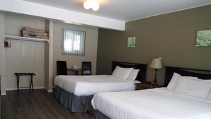 Habitación de hotel con dos camas, una mesita, una silla, un armario y una ventana con persianas.