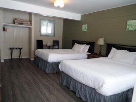 A hotel room with two beds, a small table, a chair, a wardrobe, and a window with blinds.