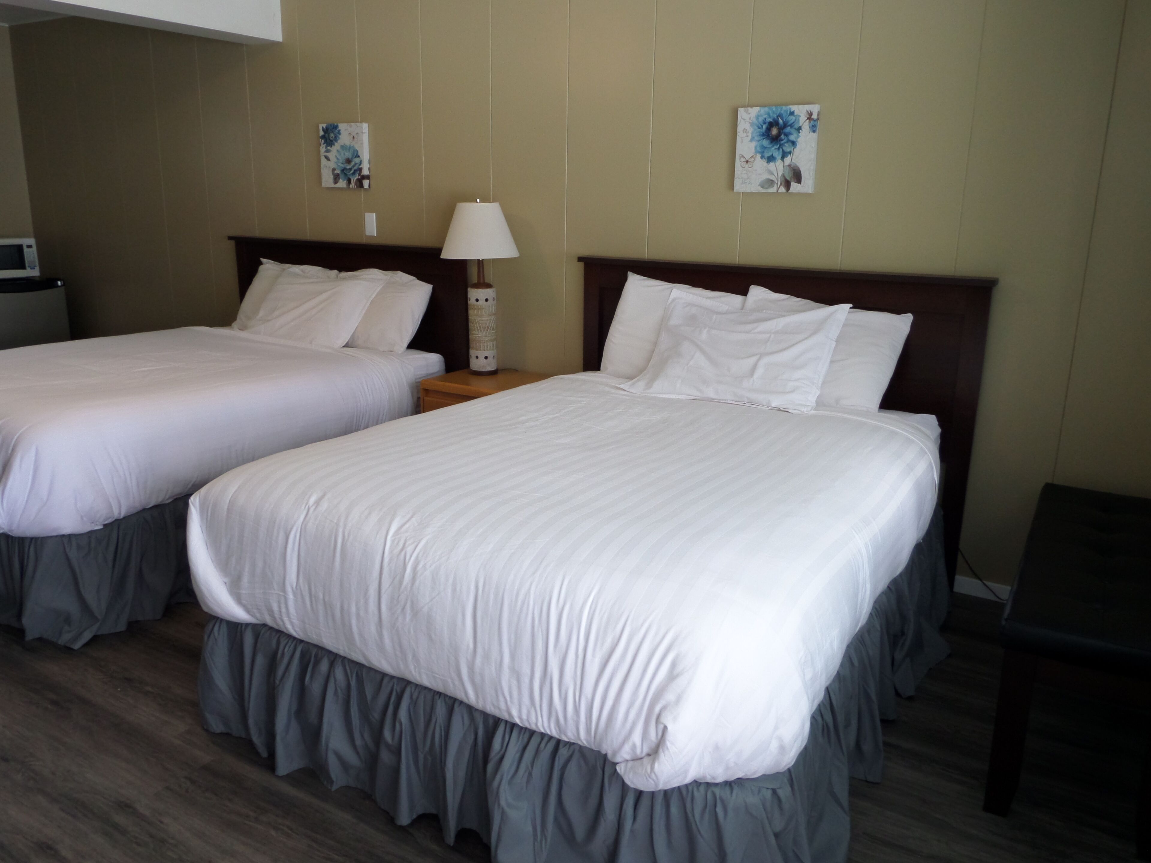 A hotel room with two single beds, a bedside table with a lamp, and a small table with a microwave.