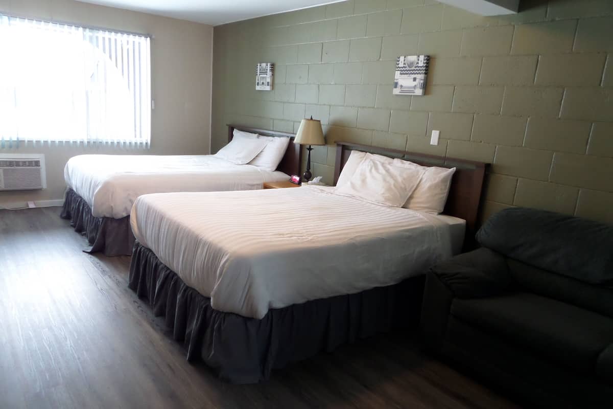 A hotel room with two beds, a sofa, a lamp, and a window with blinds.