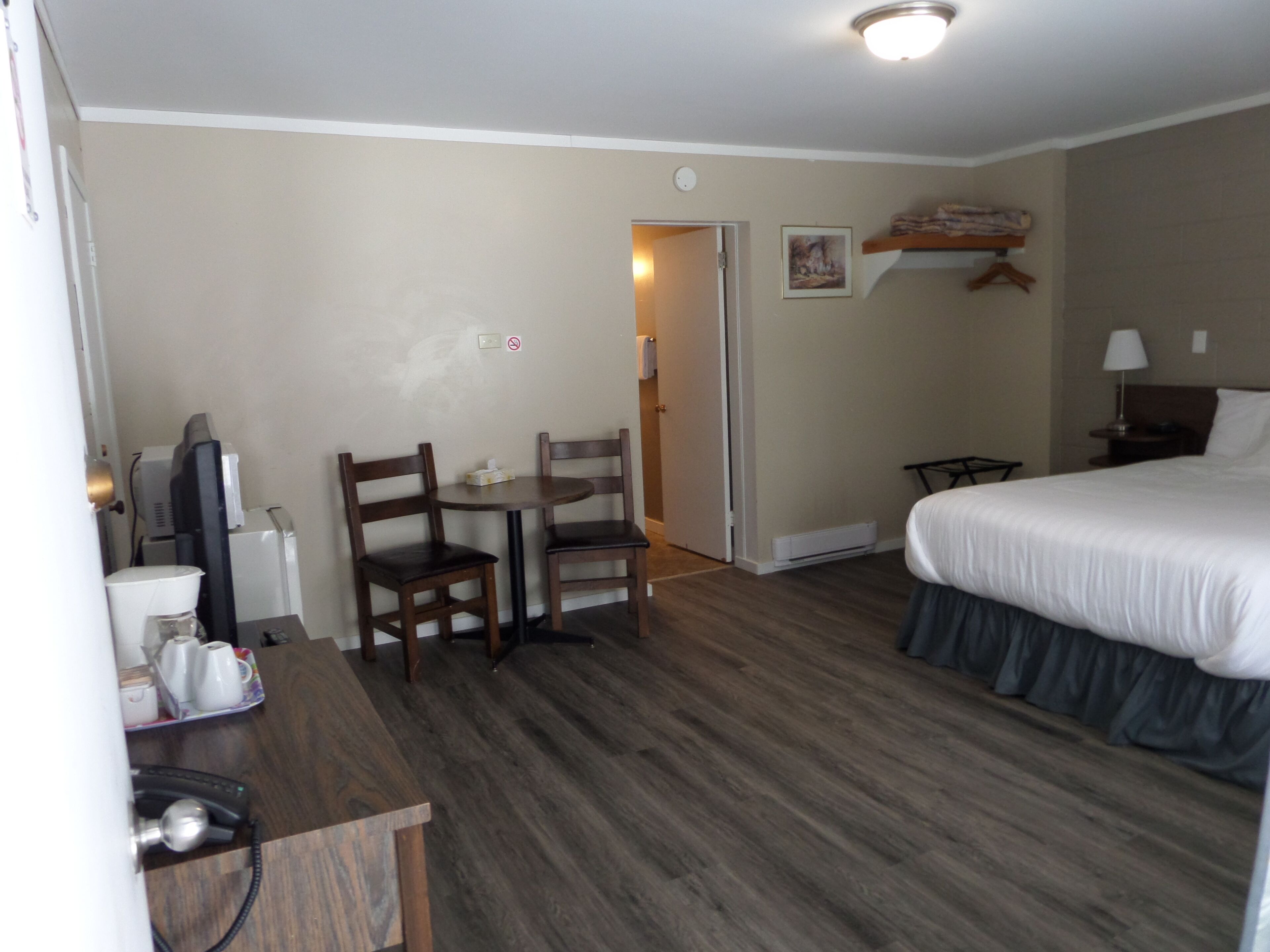 A hotel room with a bed, a desk with a chair, a small table, a television, and a heater.