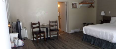 A hotel room with a bed, a desk with a chair, a small table, a television, and a heater.