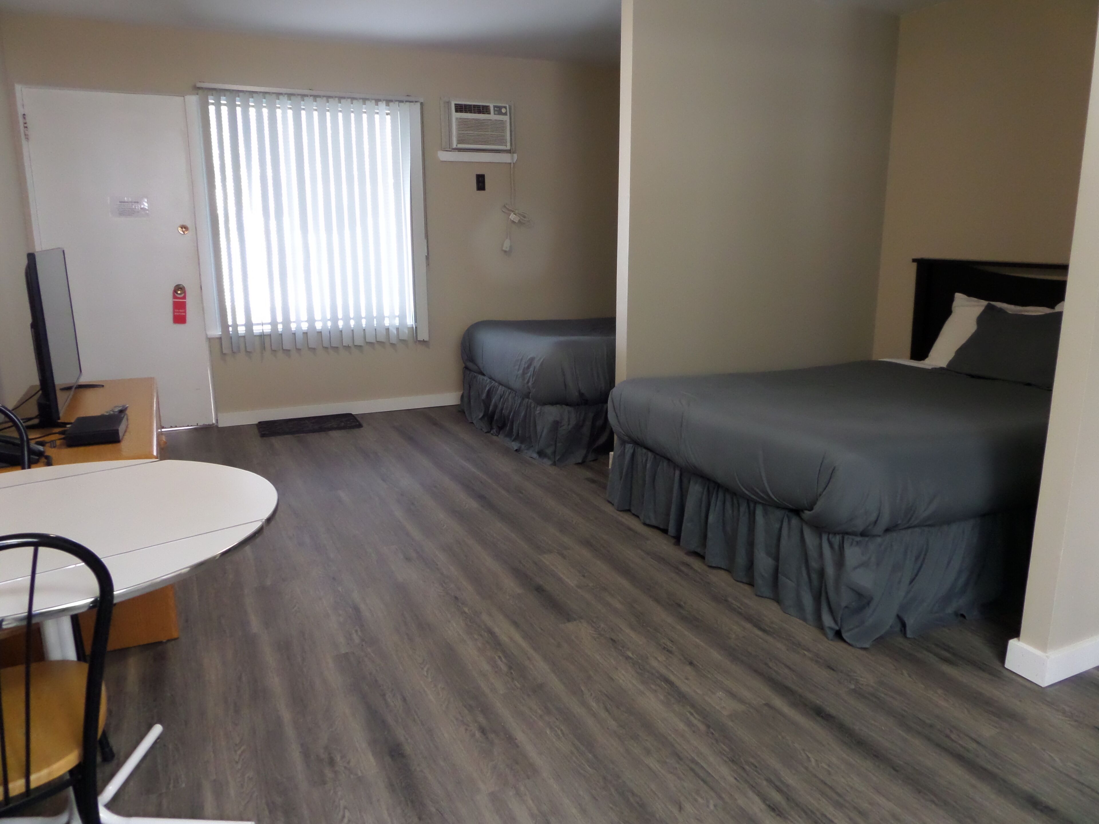 A room with two beds, a desk, a chair, a TV, and a window with blinds.