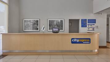 A reception desk with a CityExpress Hotels logo, framed black and white photographs on the wall, and informational signs.