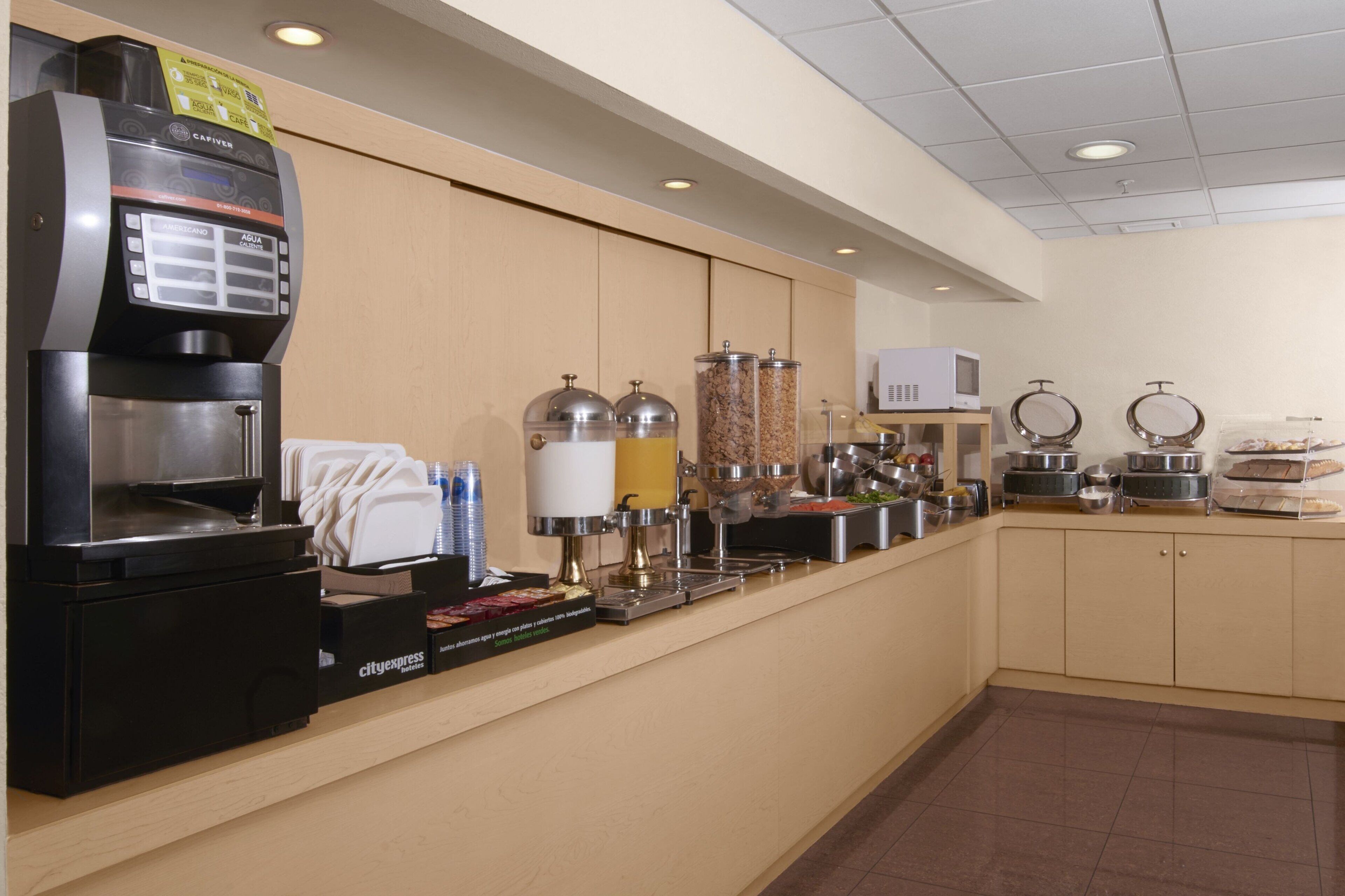 A self-service breakfast station with a coffee machine, beverage dispensers, and food containers.