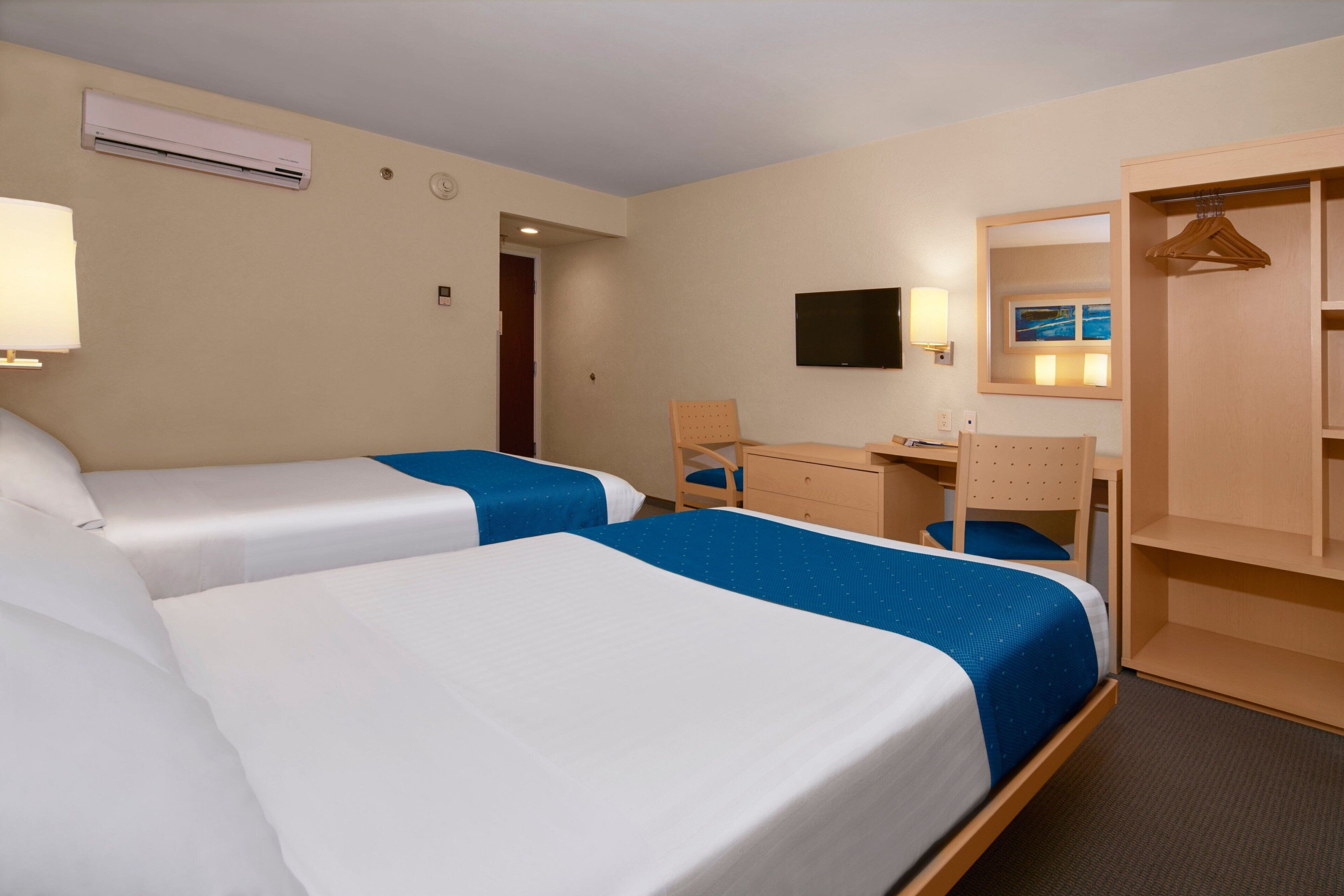 Una habitación de hotel con dos camas, un escritorio, una silla, un televisor y un armario.